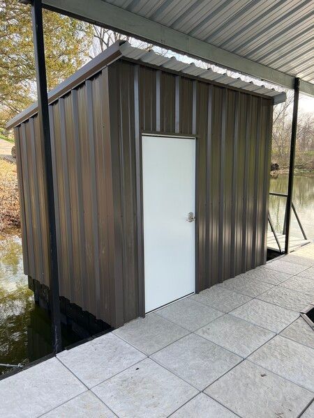 Small brown metal shed with a white door beside a covered outdoor walkway.