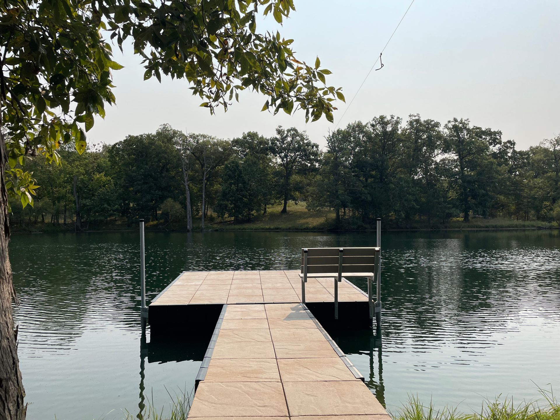 Wooden dock extending into a calm lake, with trees reflected on the water under a clear sky.