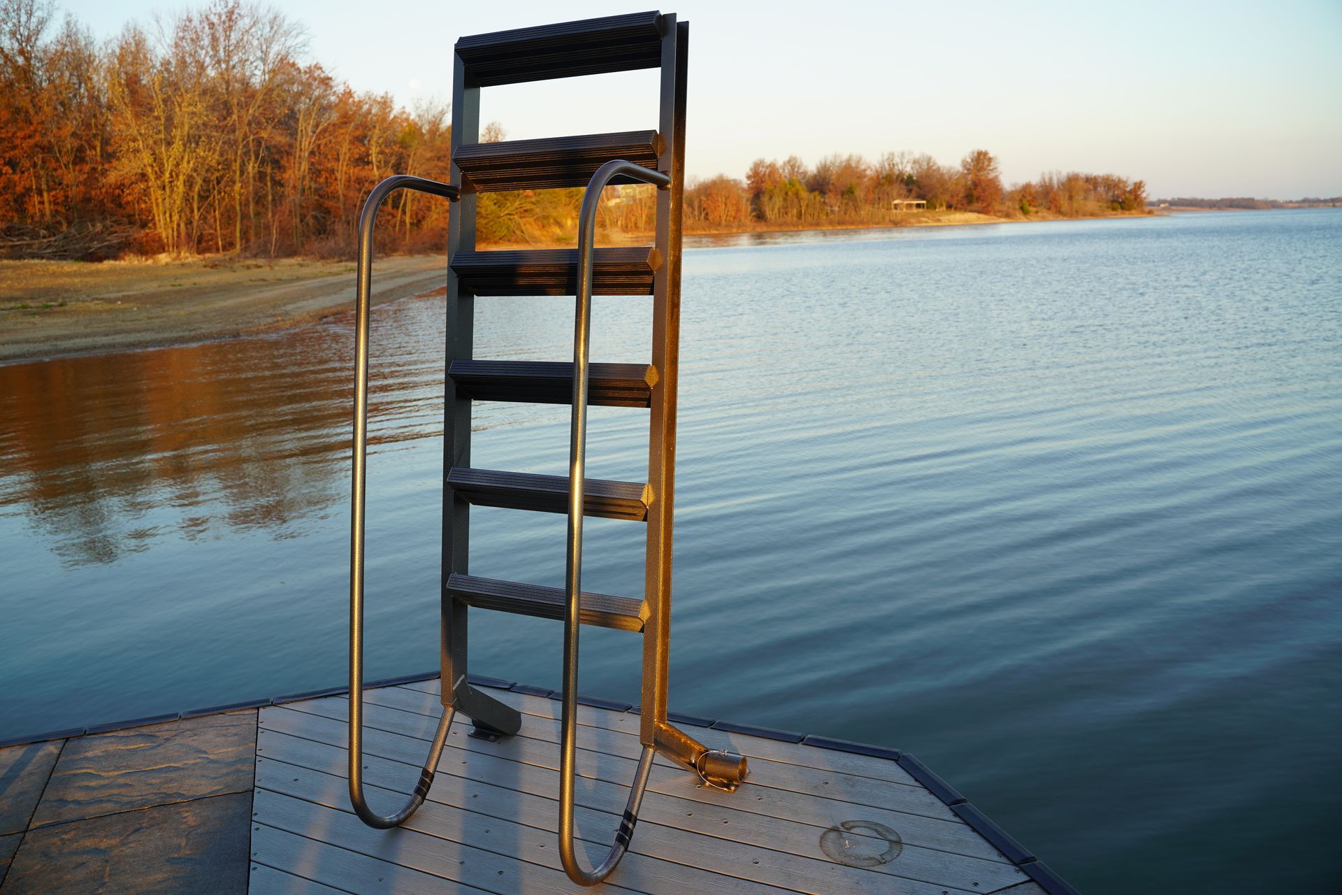 Ladder on a dock leading into a calm lake beside autumn trees at sunset