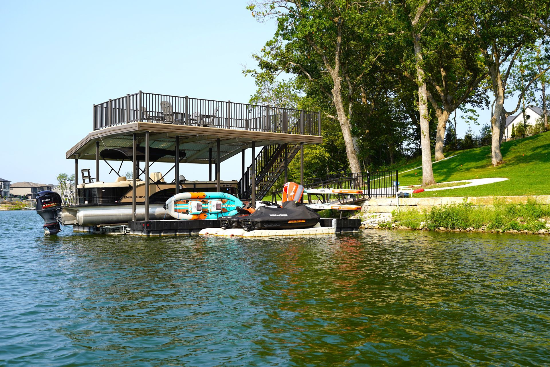 Dock by a lake with kayaks, under trees beside a grassy shoreline