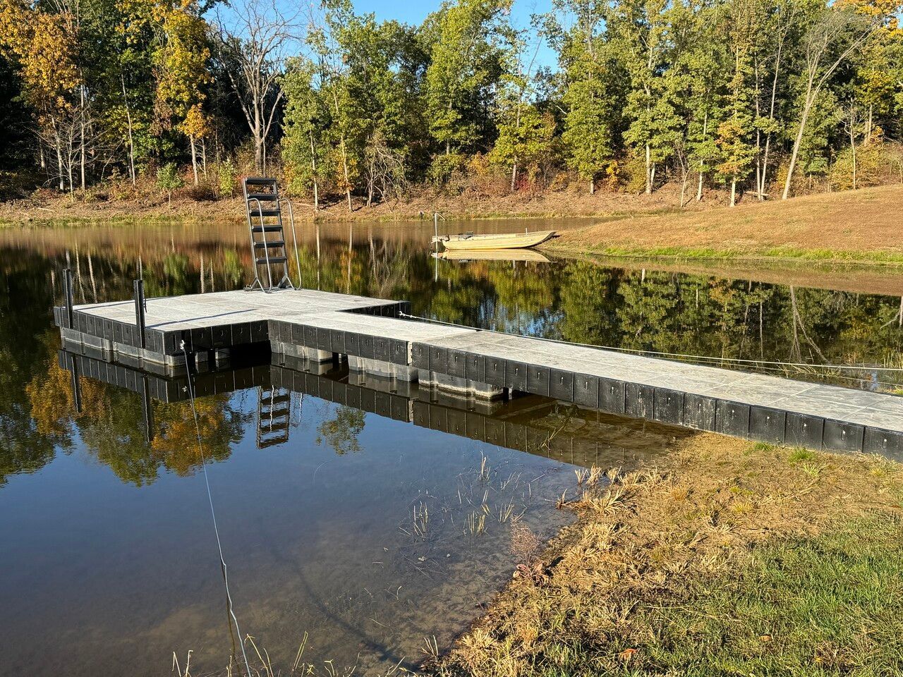 Small dock extending into a calm pond, with autumn trees and clear reflections on the water