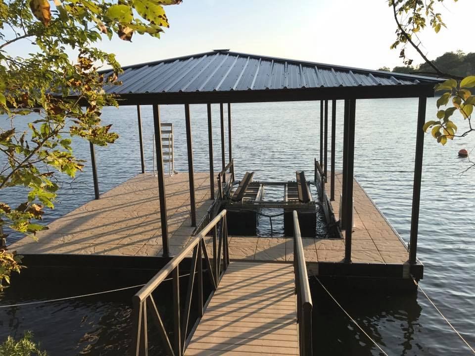 Wooden dock with a covered gazebo extending into a calm lake, framed by leafy branches