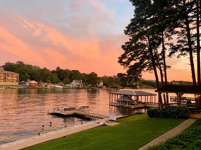 Sunset over a calm lakeside with docks, boats, and trees along the shore