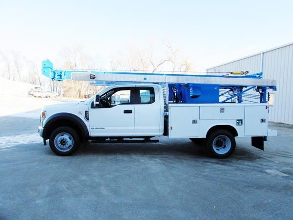A well digger truck equipped with a blue ladder is parked outside a commercial water well service facility.