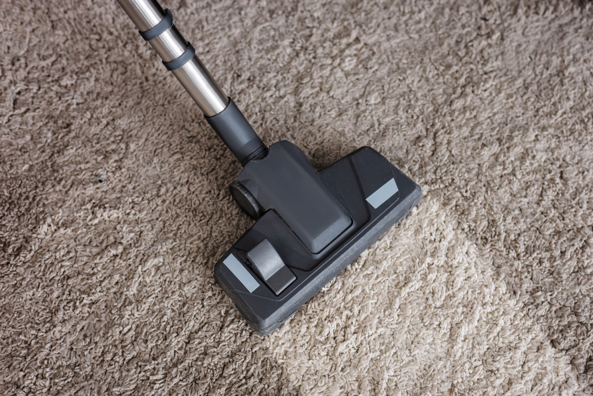 Carpet cleaning vacuum head removing dirt from soft beige carpet in residential home.