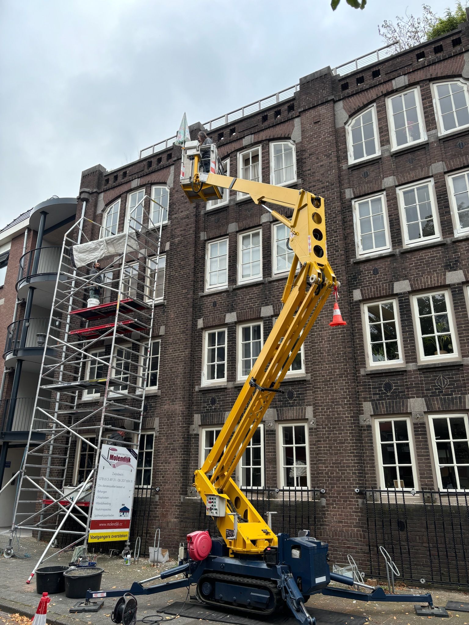 Gele lift die naar een bakstenen gebouw leidt, persoon in de lift, steiger naast een gebouw.