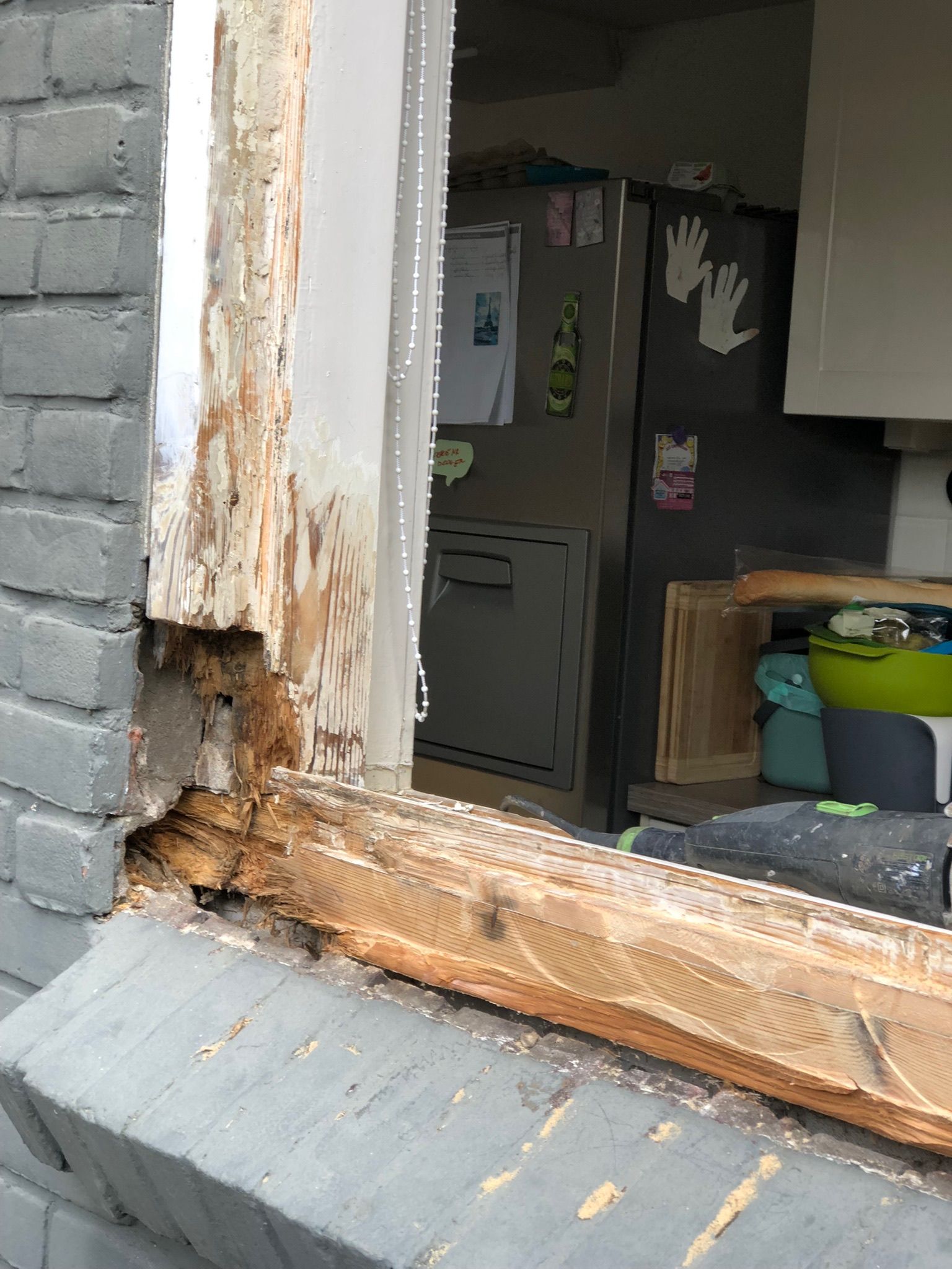 Beschadigd houten raamkozijn met rotte delen en zichtbare bakstenen aan de buitenkant.