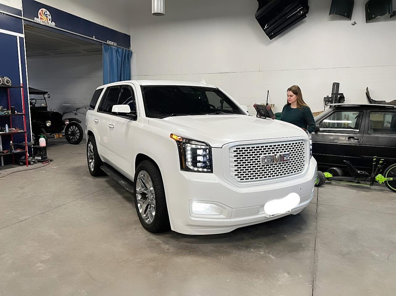 A woman is standing next to a white suv in a garage.