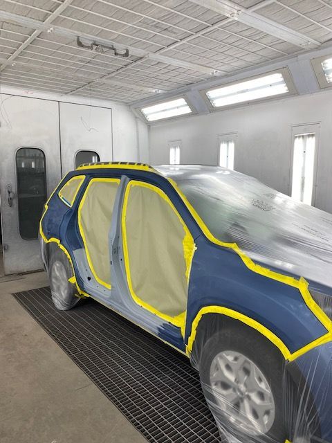 Car in a paint booth, covered in plastic and masking tape, ready for repainting.