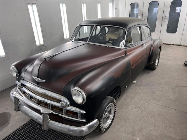 Classic black and maroon Chevrolet car in a paint booth.