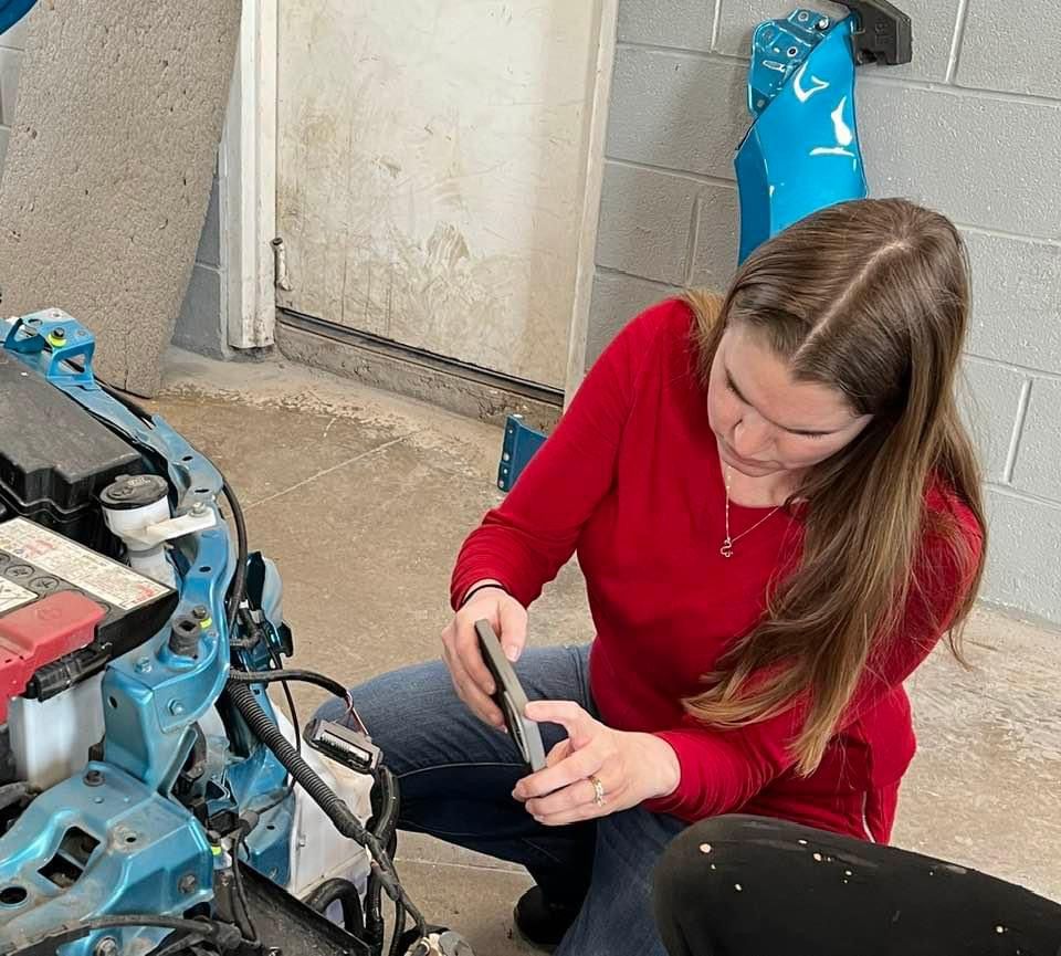 A woman in a red shirt is working on a car