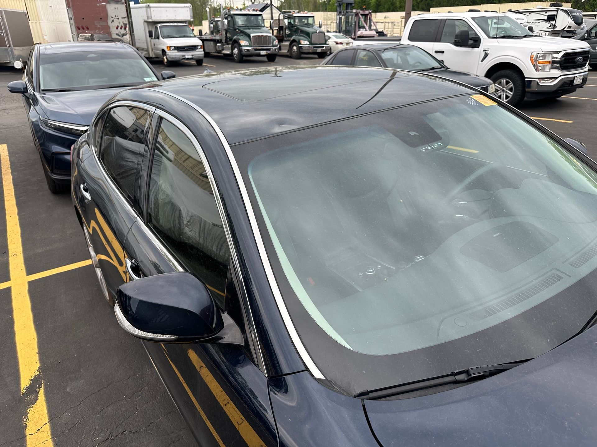 Black sedan parked in a lot with a white truck and other cars in the background