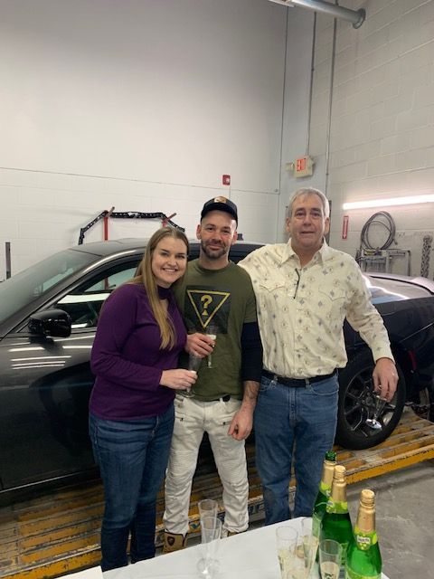 A group of people are posing for a picture in front of a car.
