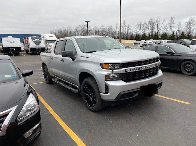 A silver truck is parked in a parking lot next to a black car.