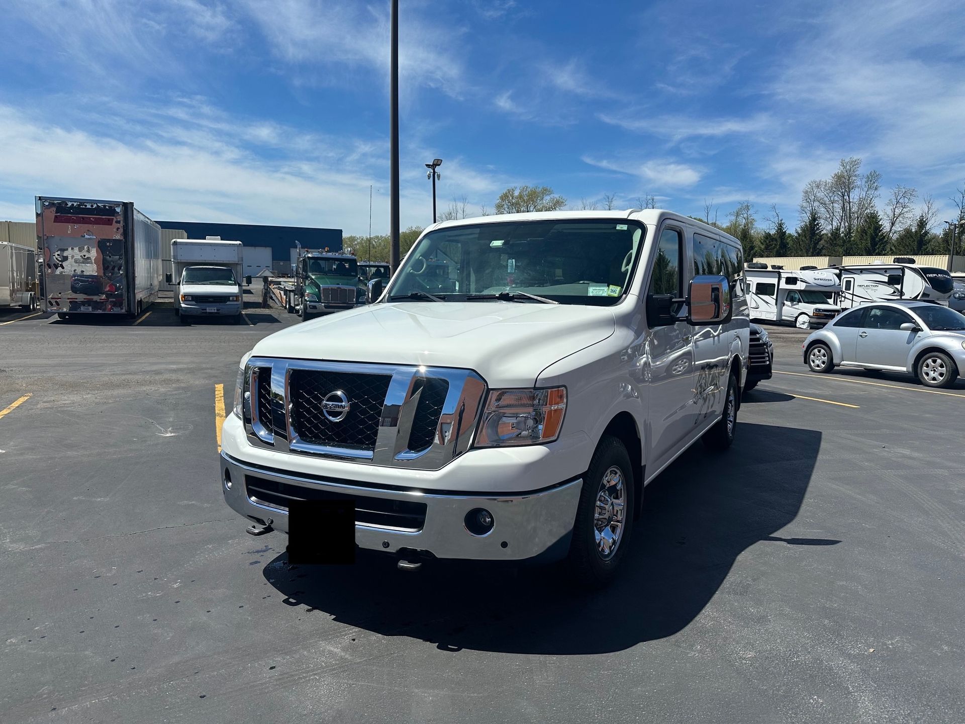 White Nissan pickup truck parked in a sunny lot with other vehicles and trucks in the background
