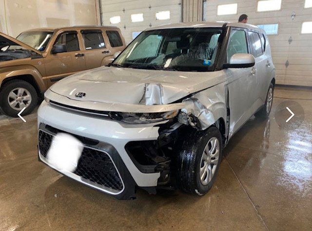 A white car with a damaged front end is parked in a garage.