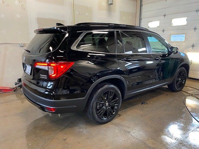 A black honda pilot is parked in a garage next to a garage door.