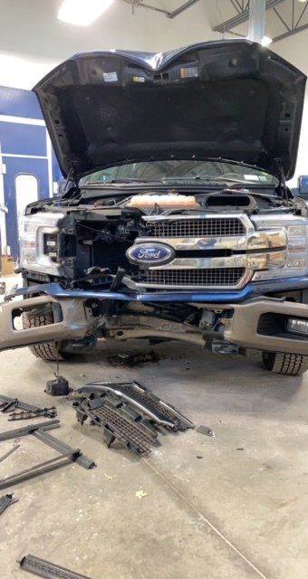 A ford truck is being repaired in a garage with the hood open.