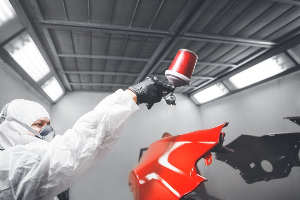 A man is spray painting a red car bumper in a paint booth.