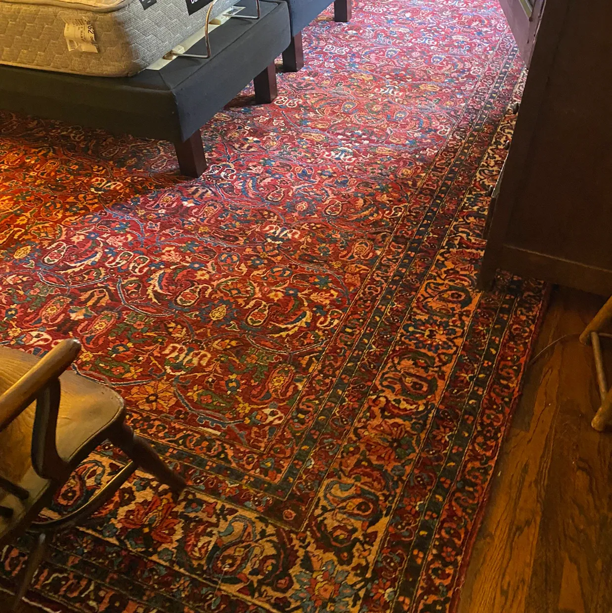 Colorful patterned rug in a room with wood flooring and chair legs visible.
