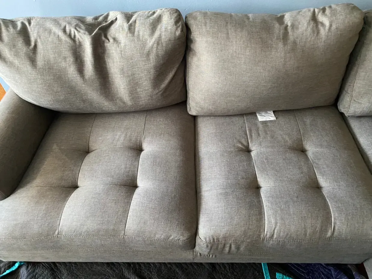 Gray fabric sofa with tufted seat cushions and a small white tag on the right cushion