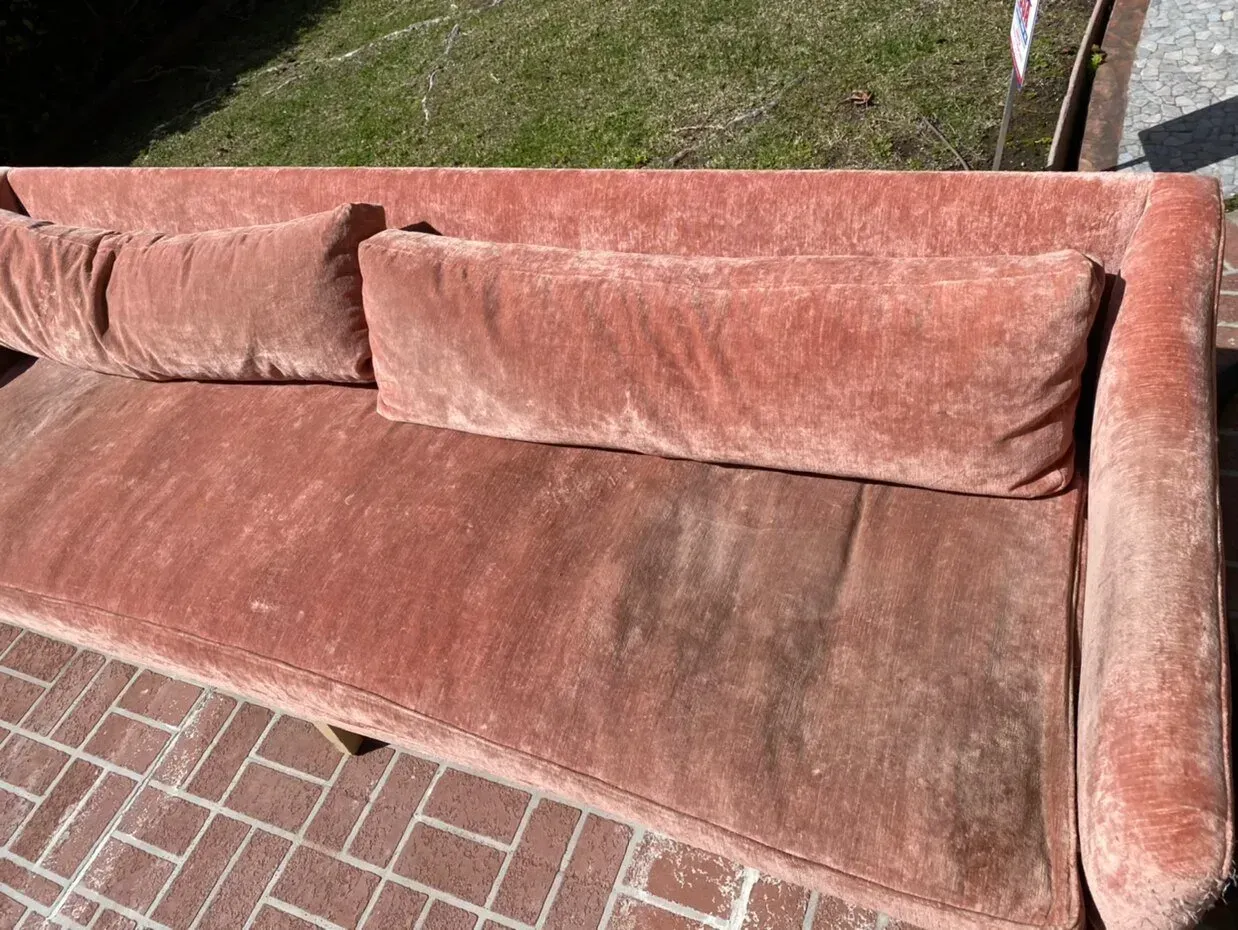 Pink velvet couch on a brick patio near a grassy lawn.
