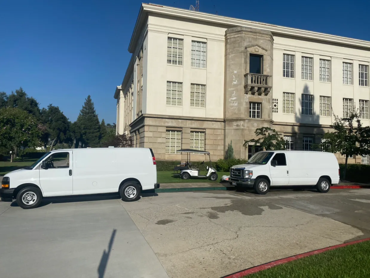 Two white vans parked in front of a large stone building under a clear blue sky.
