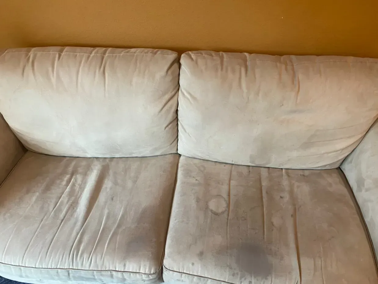 White couch cushions with dark stains and wear against a tan wall