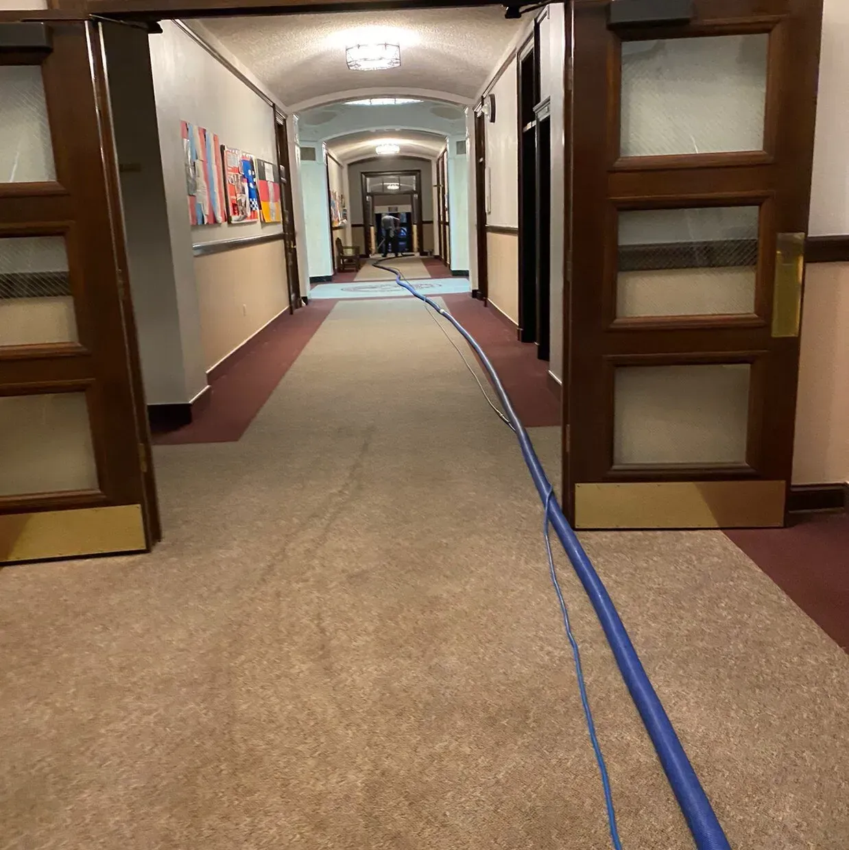 Long hallway with carpet and blue cable running down the center, seen through open wooden doorways.