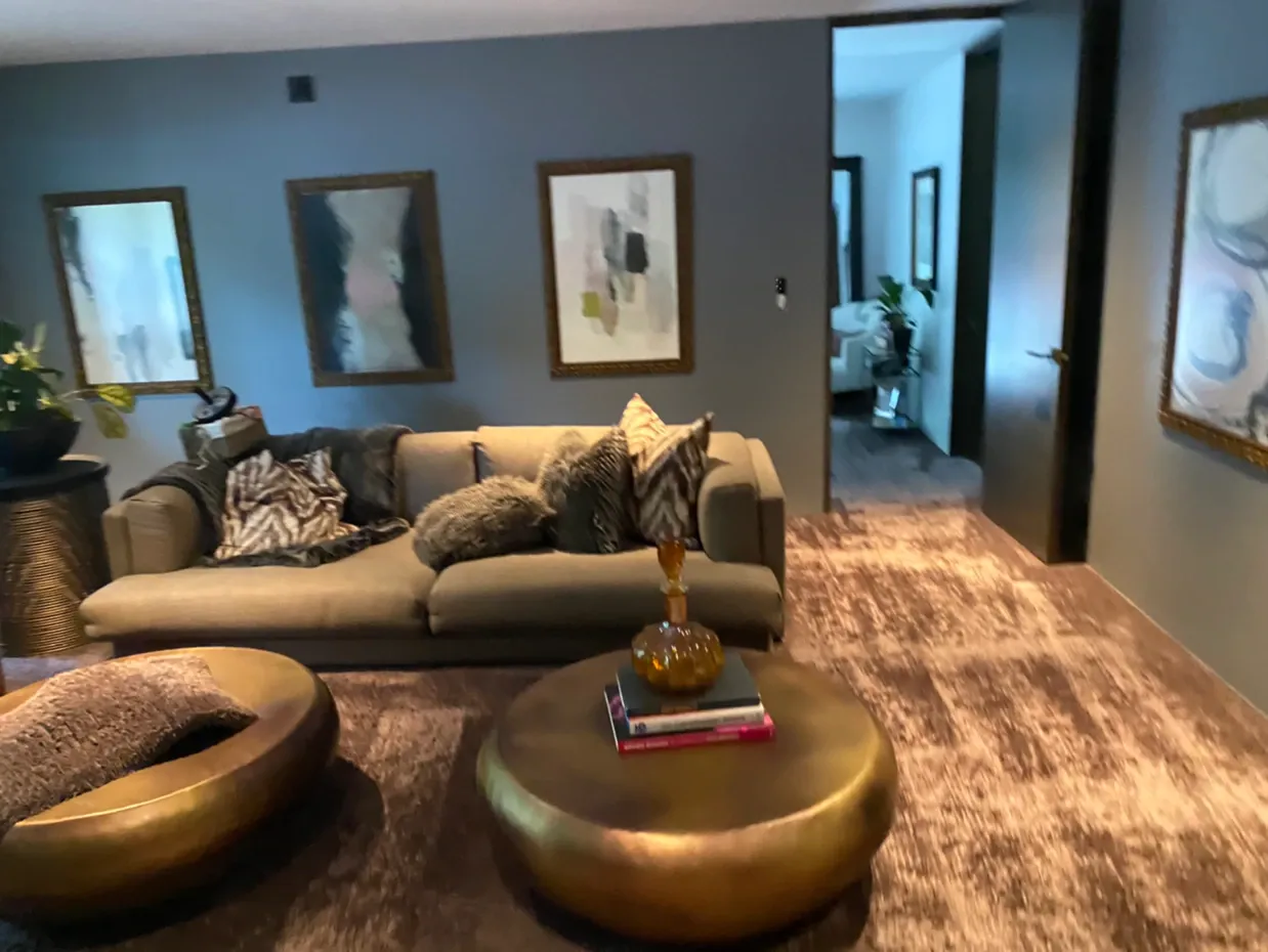 Modern living room with gray sofa, gold coffee tables, wall art, and a hallway view