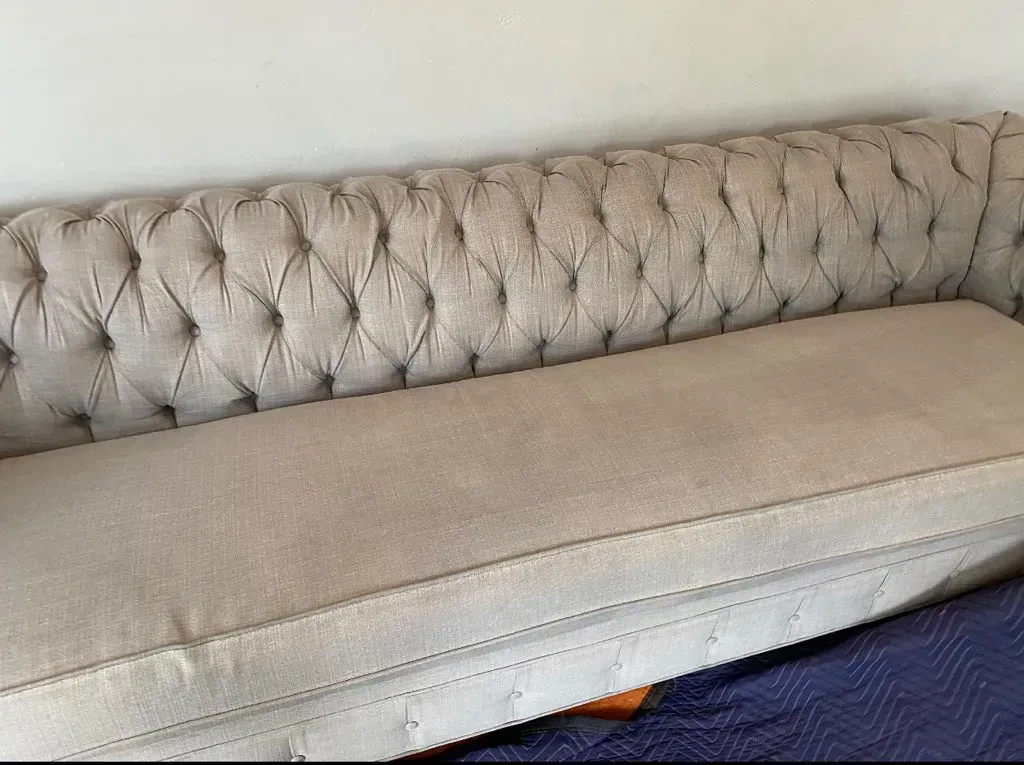 Tufted beige sofa with a light cushion and blue blanket draped along the bottom