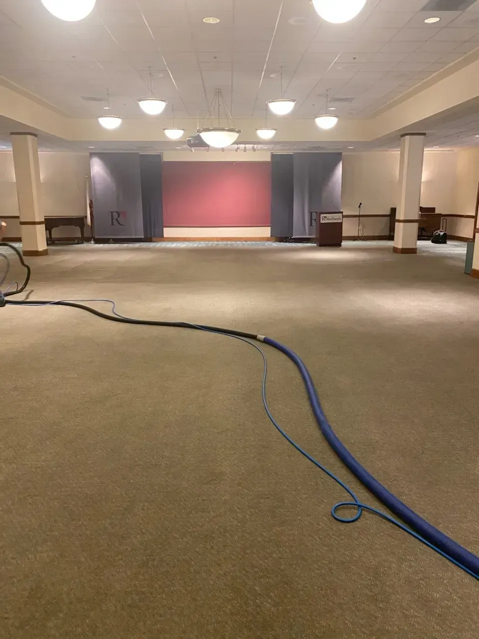 Worker vacuuming debris from a living room with ocean-view windows and rugs being laid out.