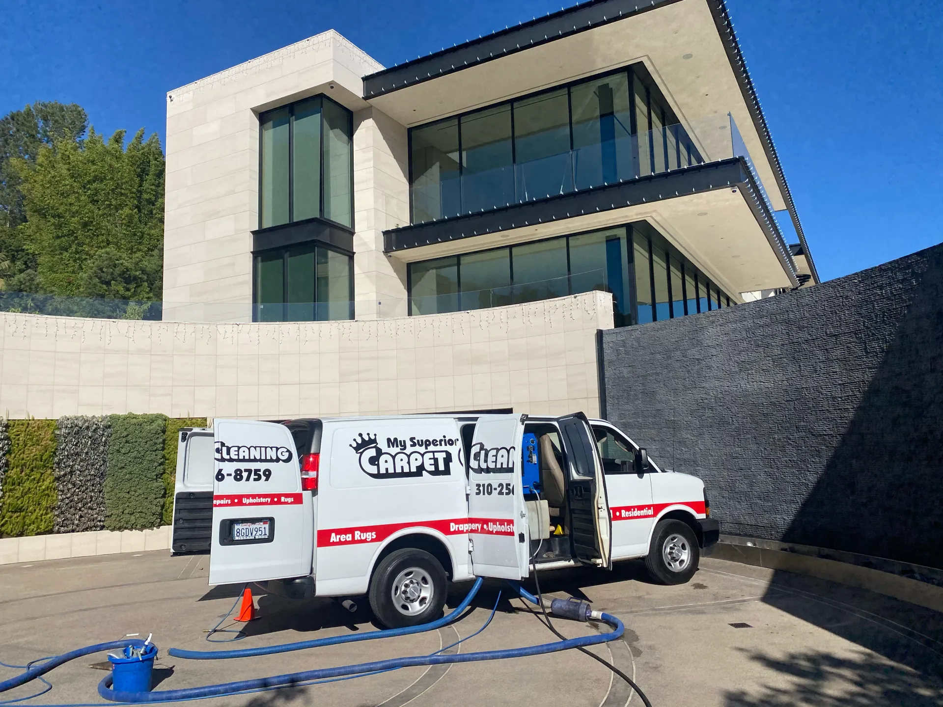 White utility van parked in front of a modern house with a black driveway wall and hose on the ground