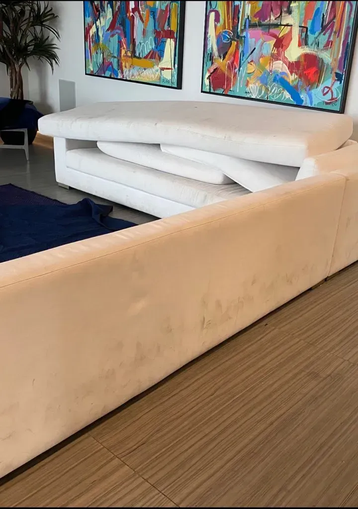 White sectional sofa with a visible stain in a modern living room, beneath colorful abstract wall art