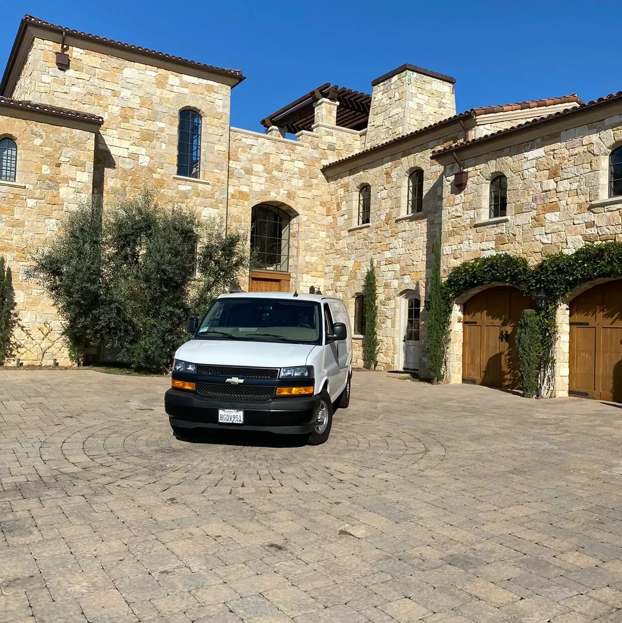 White van parked in a stone courtyard beside a rustic villa with arches and tiled roofs