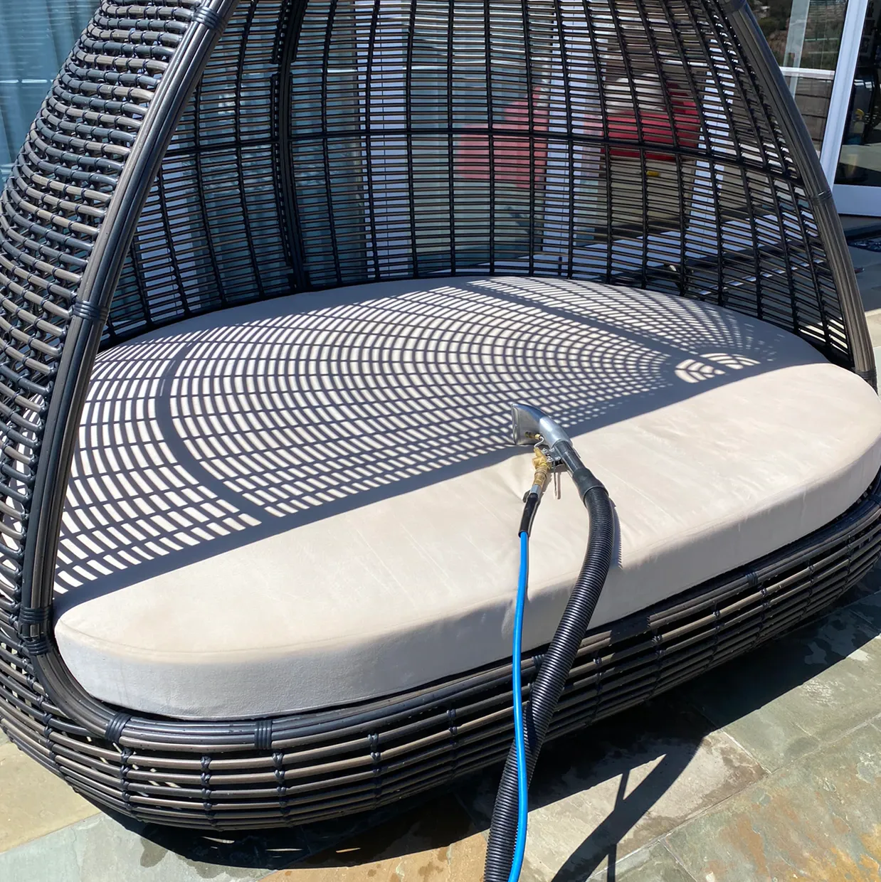 Round wicker hanging daybed with cream cushion and blue rope outdoors in sunlight