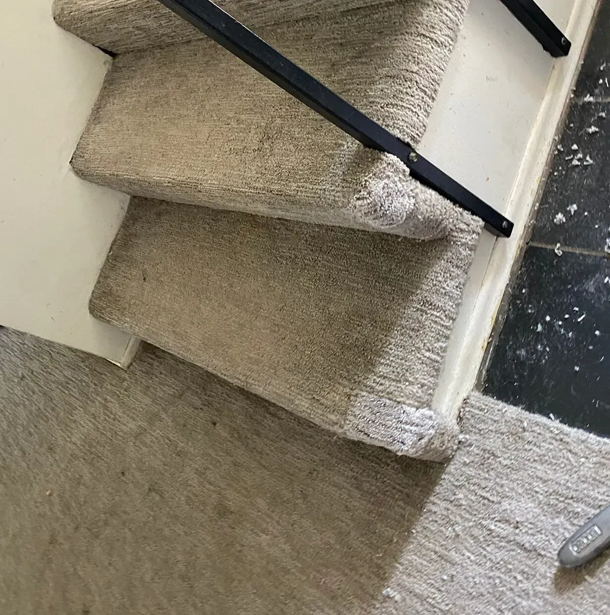 Carpeted staircase with black handrail and beige walls, viewed from the bottom landing