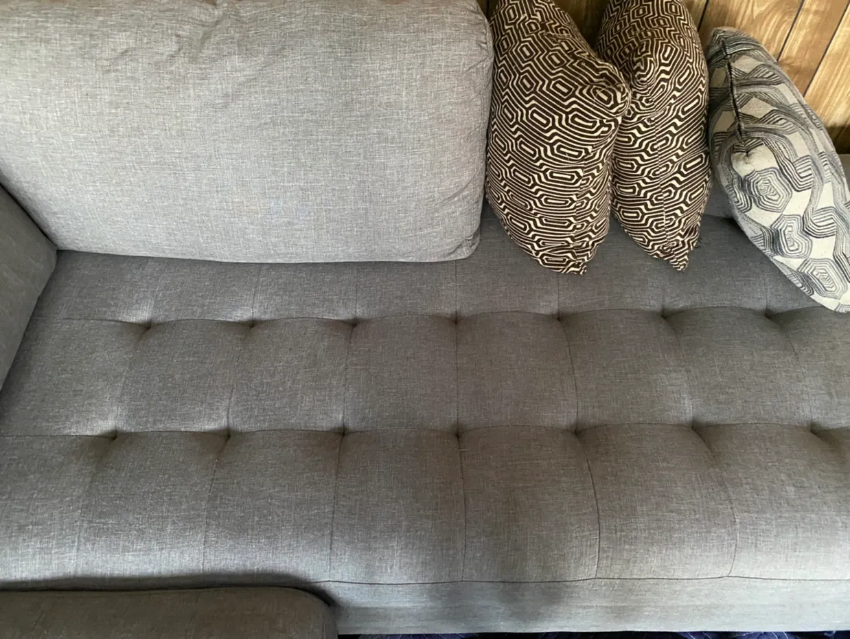 Gray tufted sofa with patterned pillows against a light gray wall