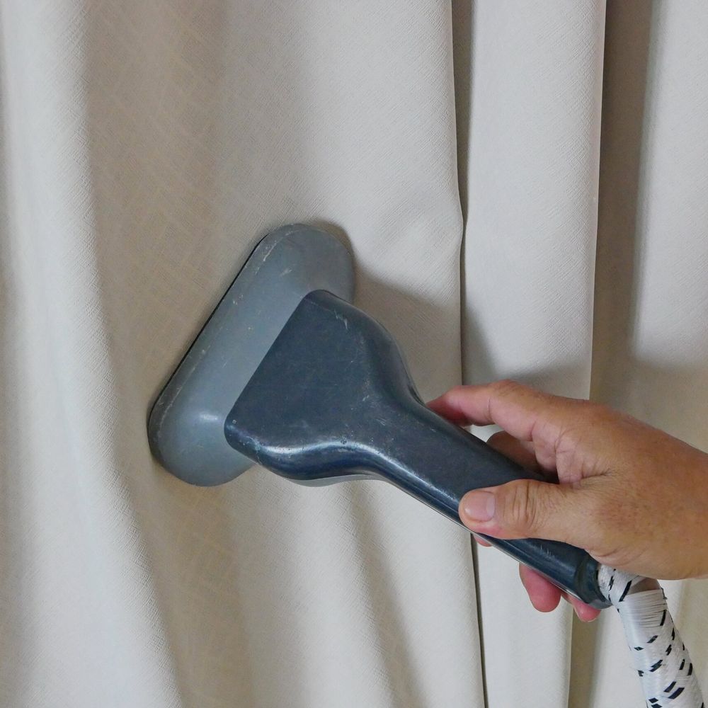 Hand-held vacuum cleaner nozzle cleaning beige curtains