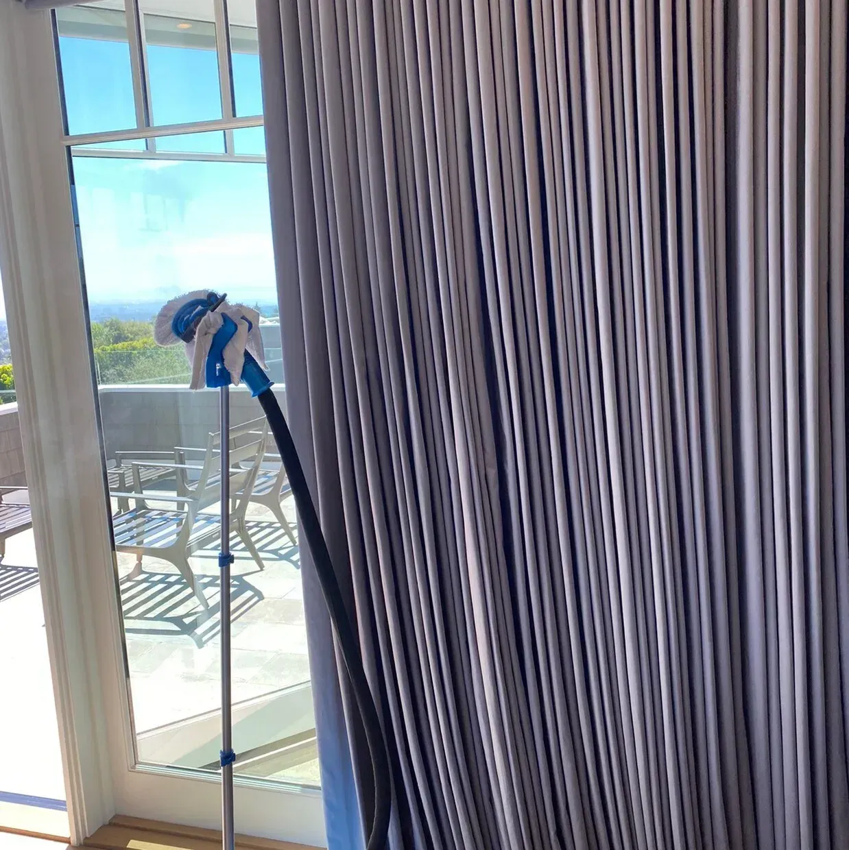 Curtained window with a blue-handled mop or vacuum near a balcony overlooking the water