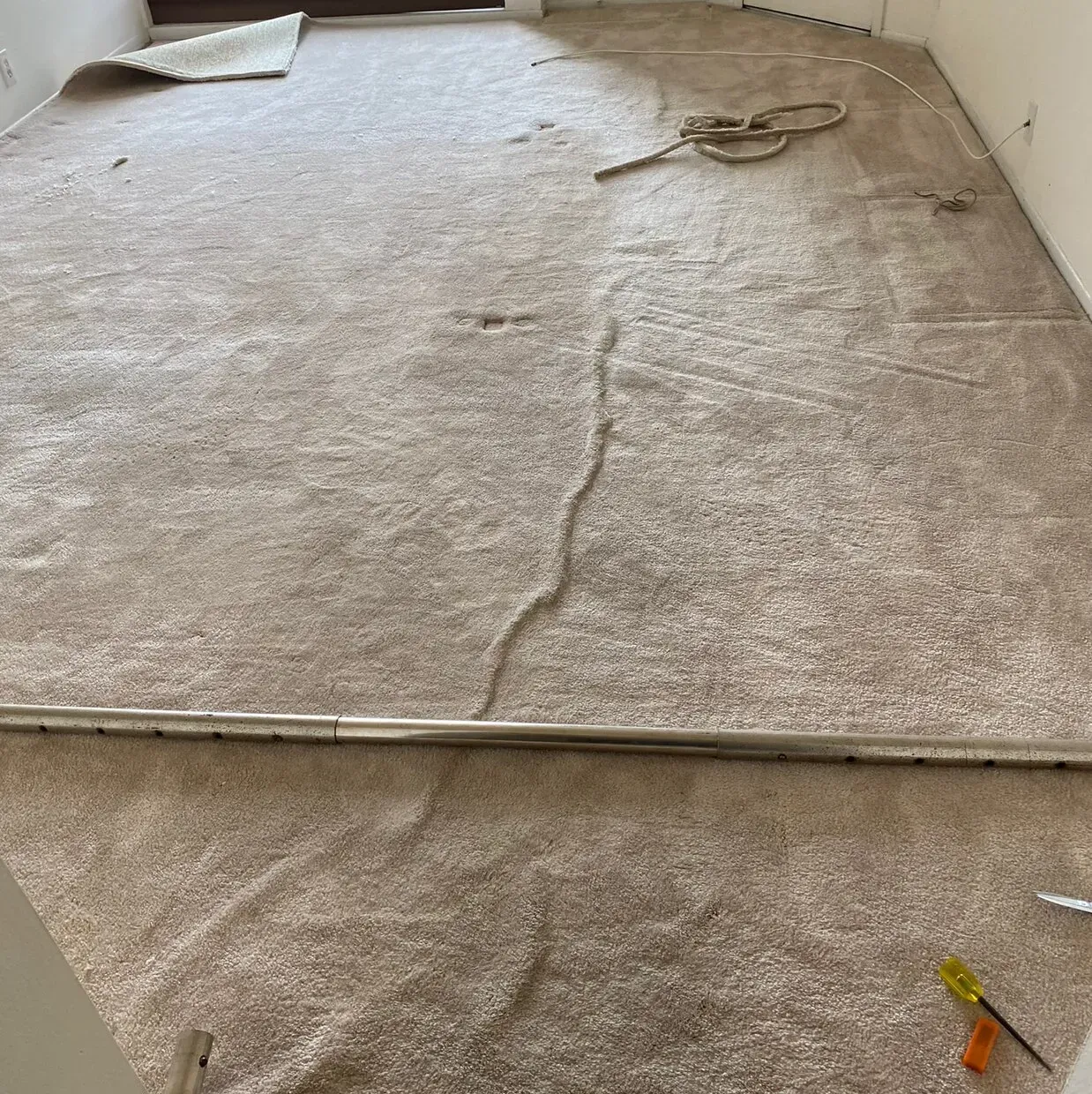 Damaged beige carpet with a long seam tear and small debris on the floor