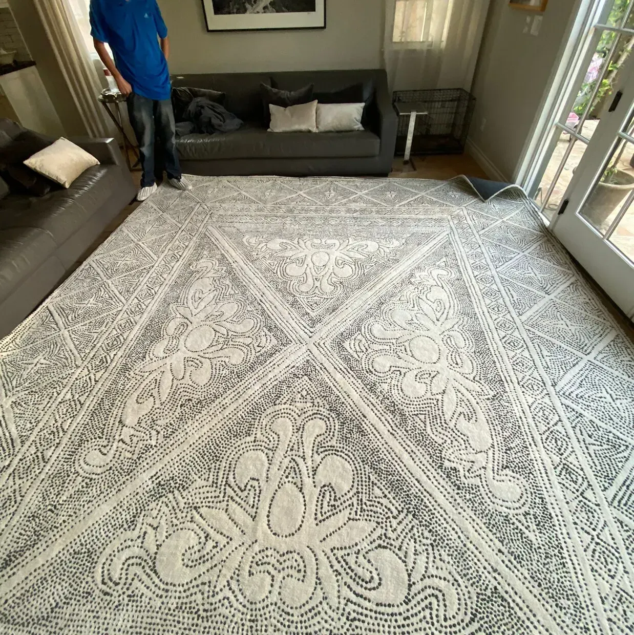 Living room with a large patterned rug, dark sofas, and a person standing near the left sofa.