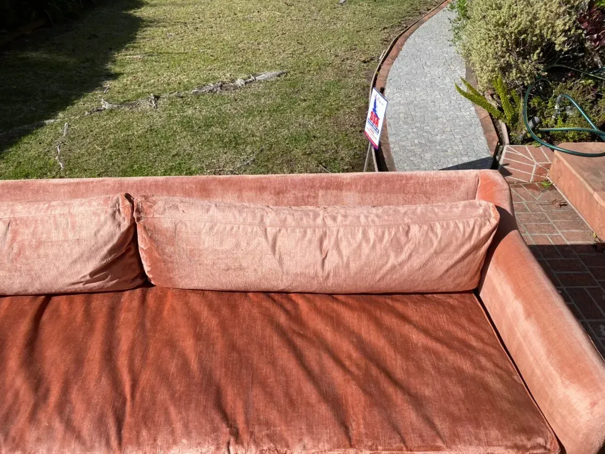 Pink outdoor sofa beside a lawn and curved garden path in sunlight