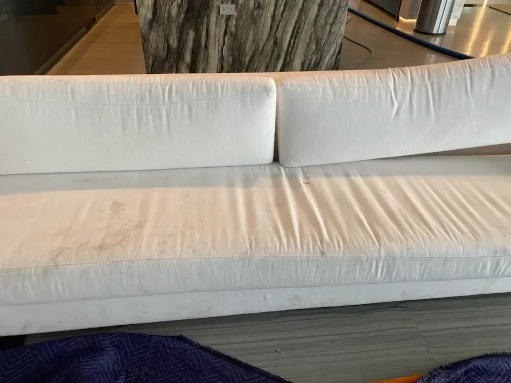 White sofa with rumpled cushions in a modern living room, with a dark rug and glass coffee table behind it