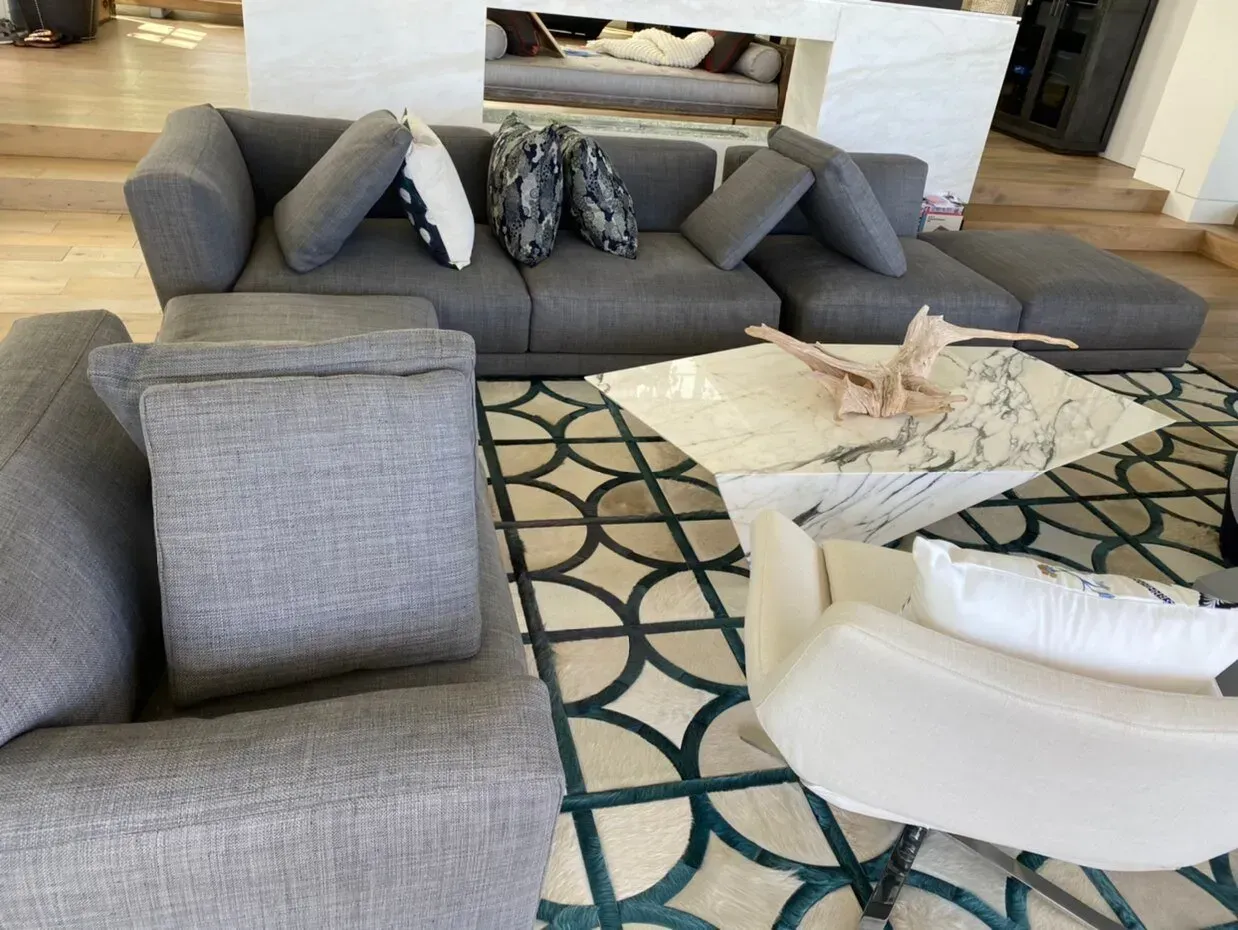 Modern living room with gray sectional sofa, patterned rug, and white chairs near a fireplace