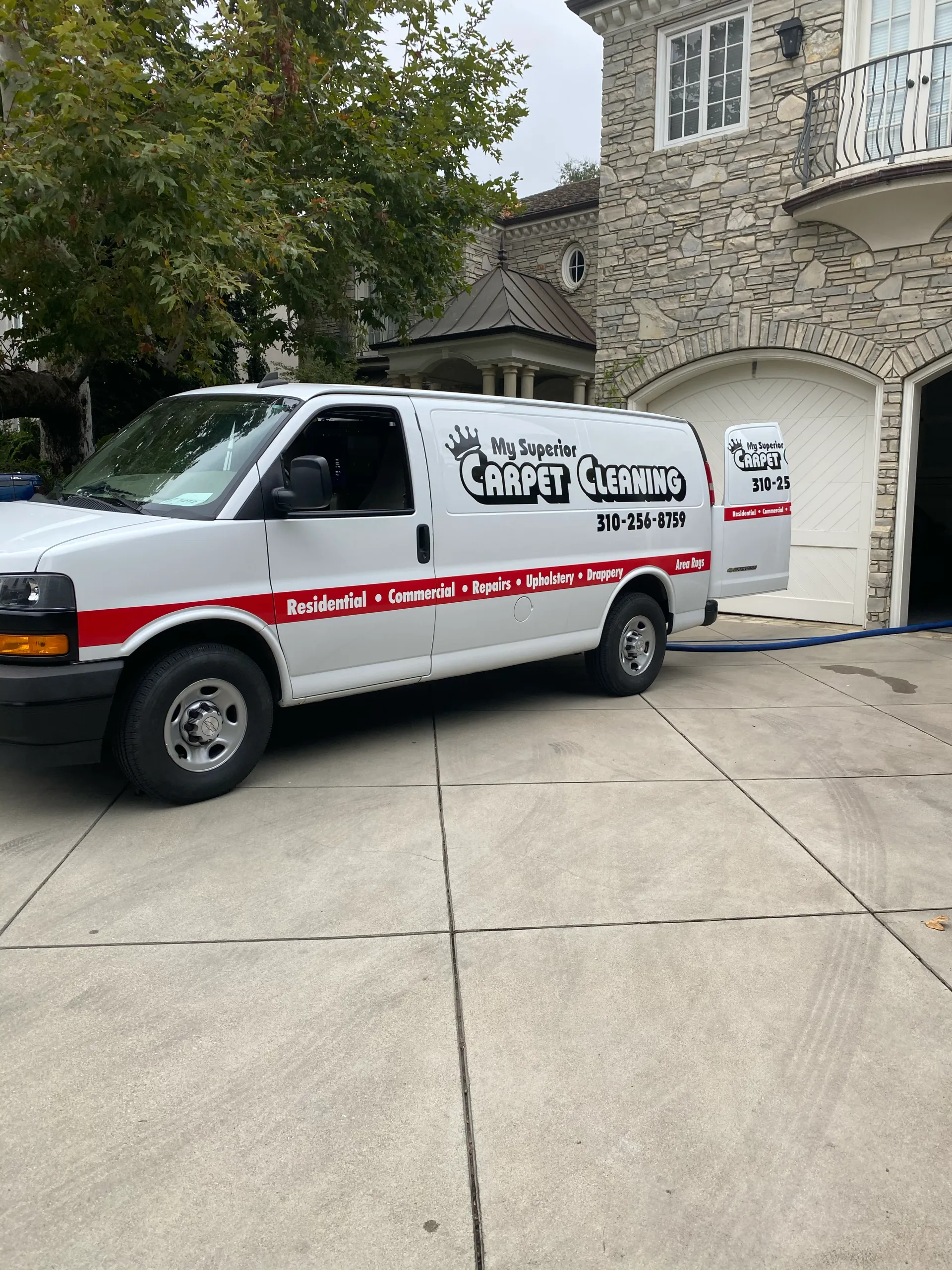 White service van with red stripe parked in a driveway beside a stone building and garage door.