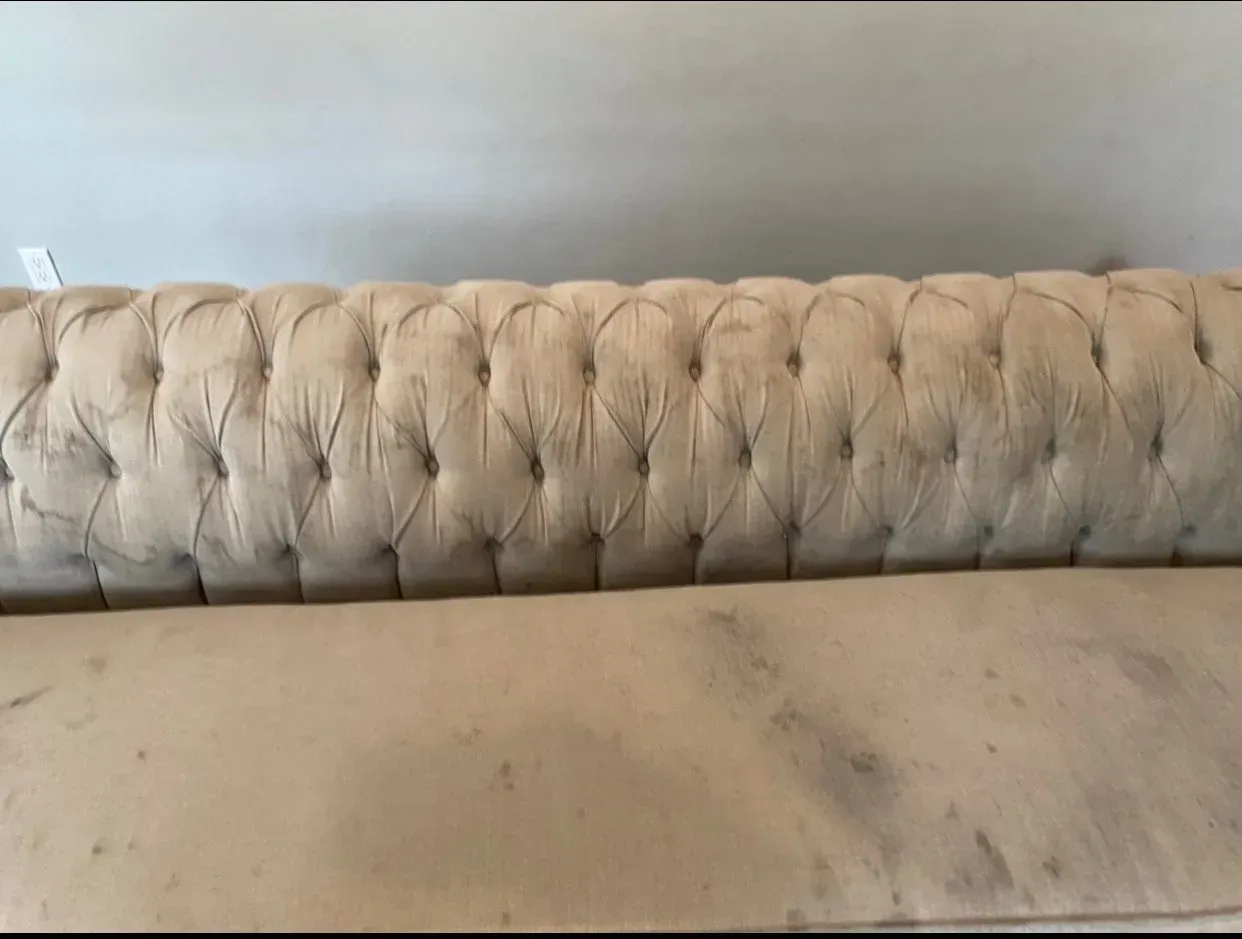 Beige tufted upholstered sofa back and seat against a light gray wall.