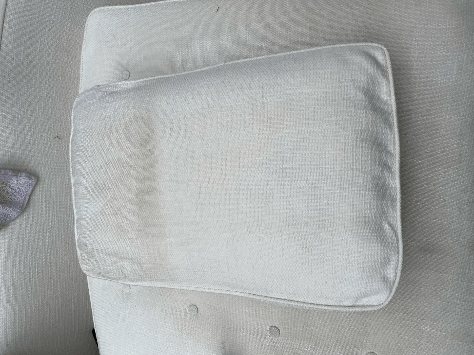 White rectangular cushion on a light gray upholstered surface.
