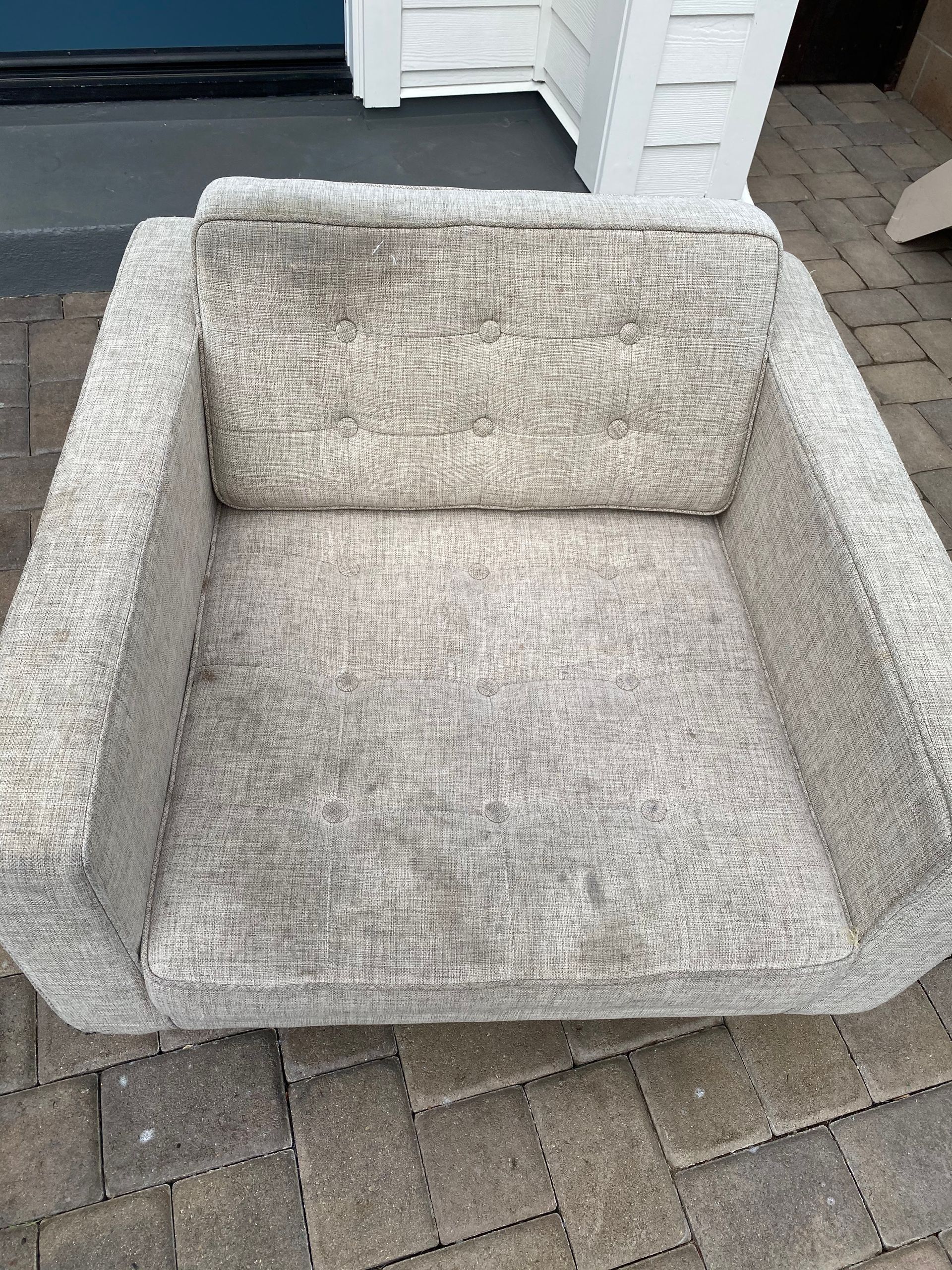 Gray upholstered armchair with wide arms on a brick patio outdoors