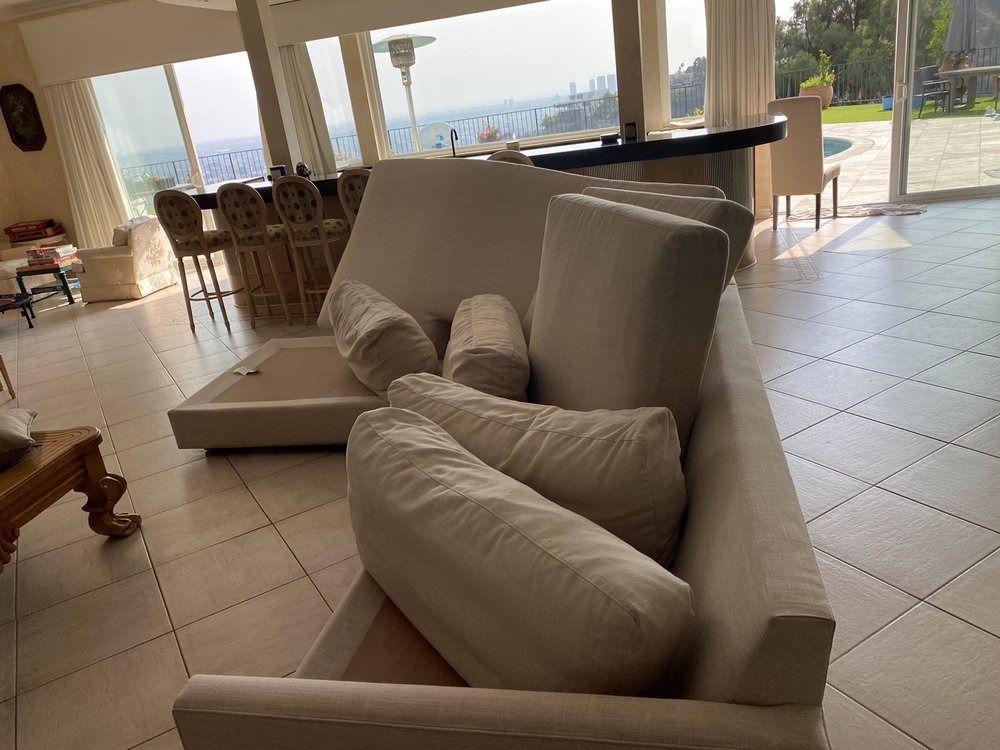 Living room with beige sofa and cushions, tiled floor, and large windows overlooking a bright outdoor view